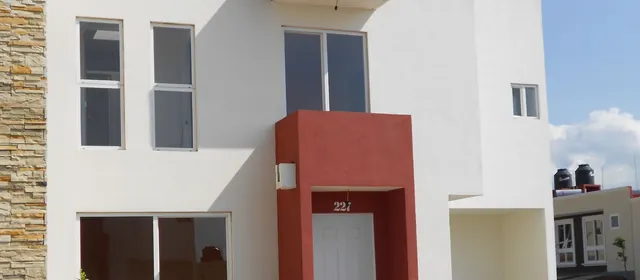 Casa habitación con acceso enmarcado en rojo y ventanas de PVC blanco