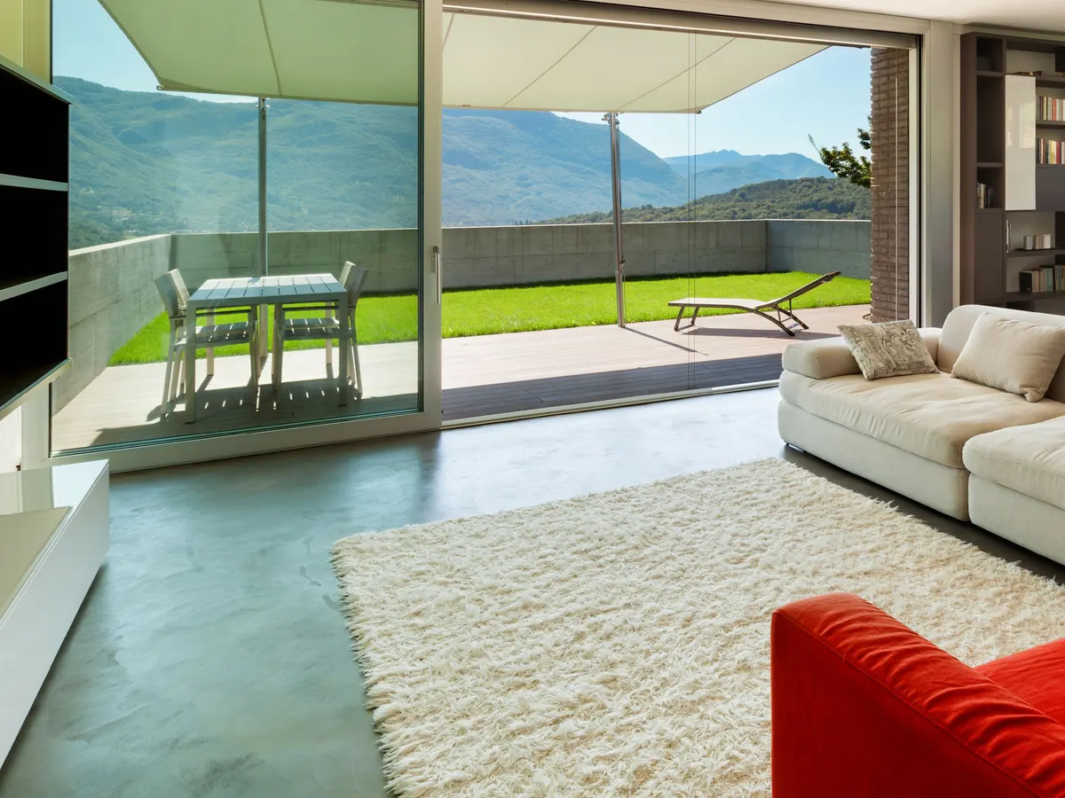 Estancia con cancelería corrediza de piso a techo abierta hacia una terraza con vista a la montaña
