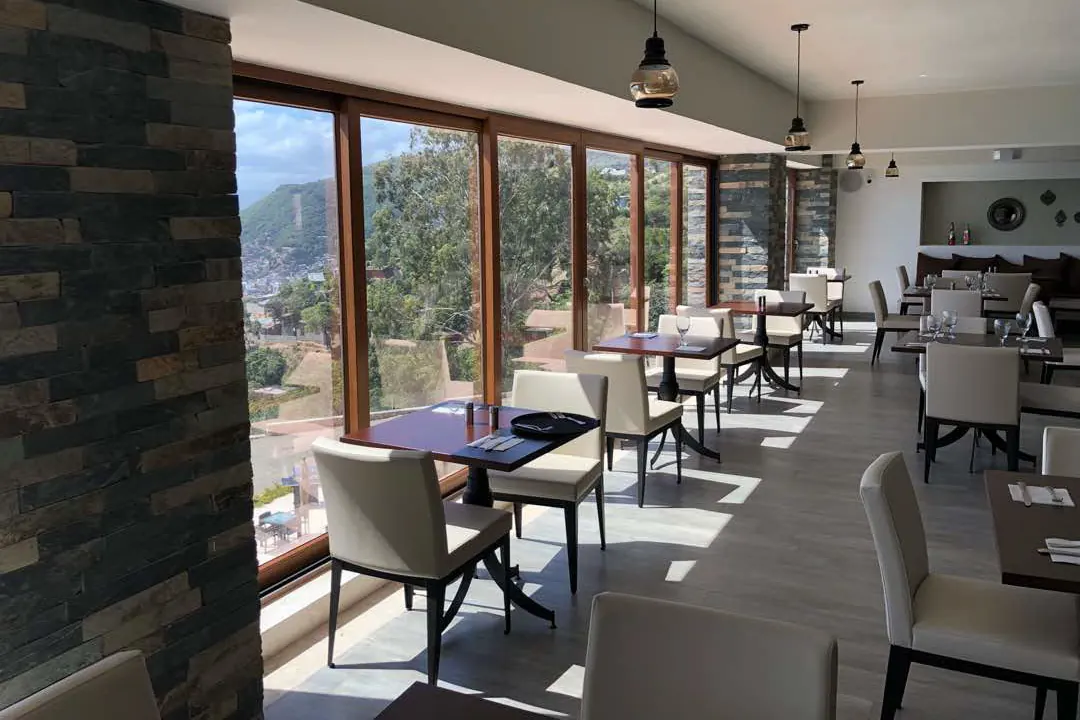 Salón de restaurante con cancelería continua de marco oscuro sobre muro de piedra