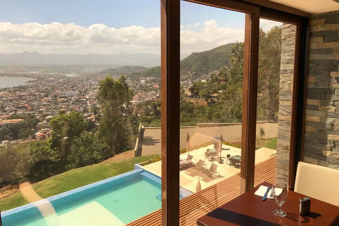 Estancia con ventanal de esquina abierto a una terraza con alberca y vista a la ciudad